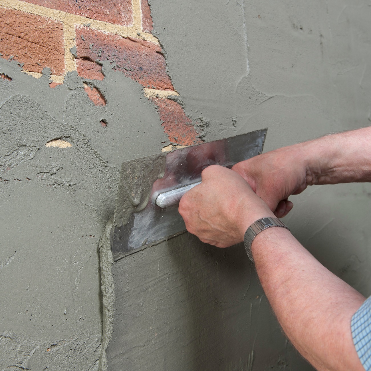 Person applying grey damp proof slurry to a brick wall with a trowel.