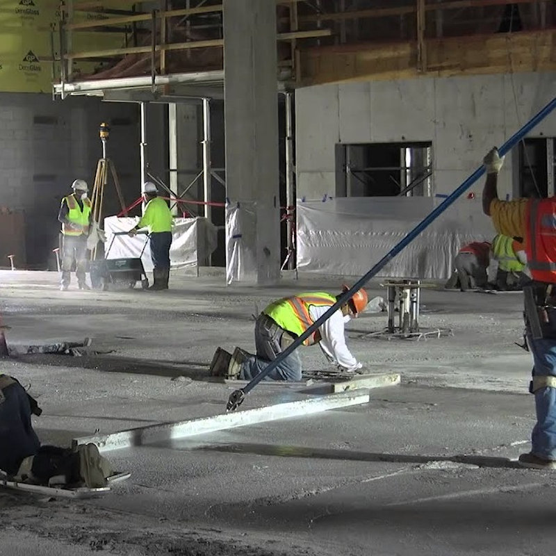 Construction workers applying a concrete hardener on a large floor surface in a building site.
