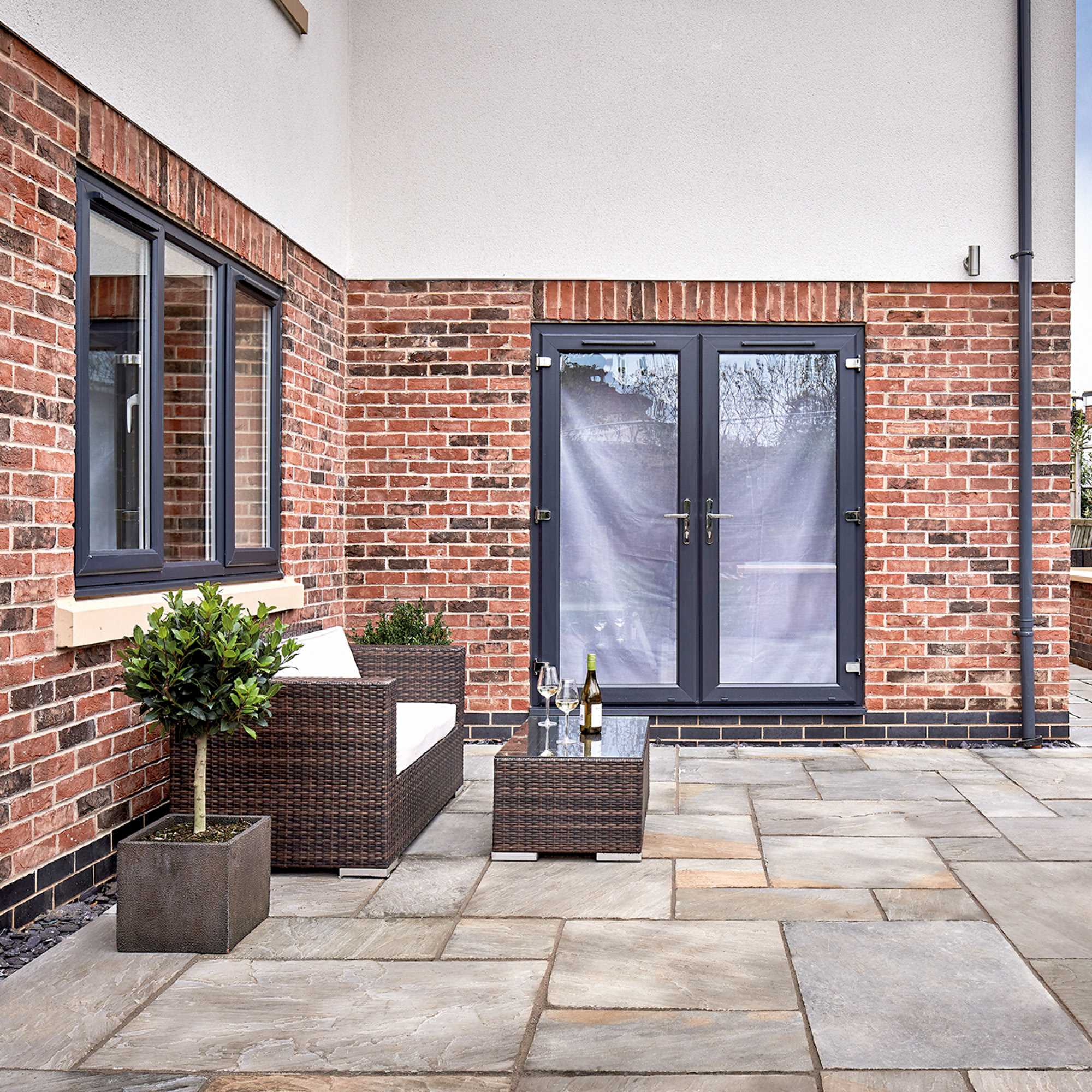 Close-up of sandstone slab patio with Sika FastFix compound in joints, modern outdoor seating and brick wall background
