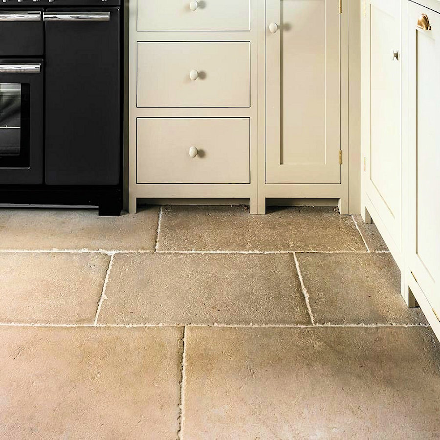Natural stone flooring in a kitchen setting with cream cabinets and a black oven.