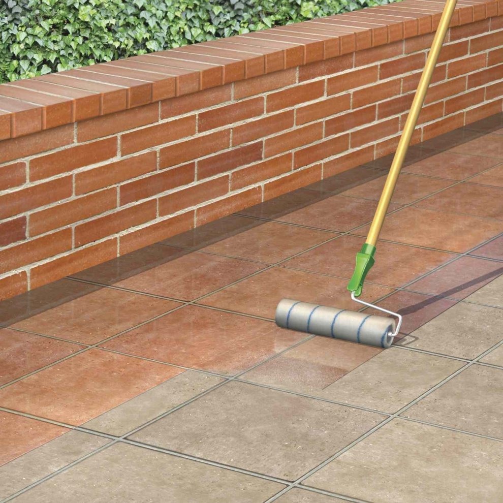 A roller applying clear paving sealer on patio tiles next to a brick wall.