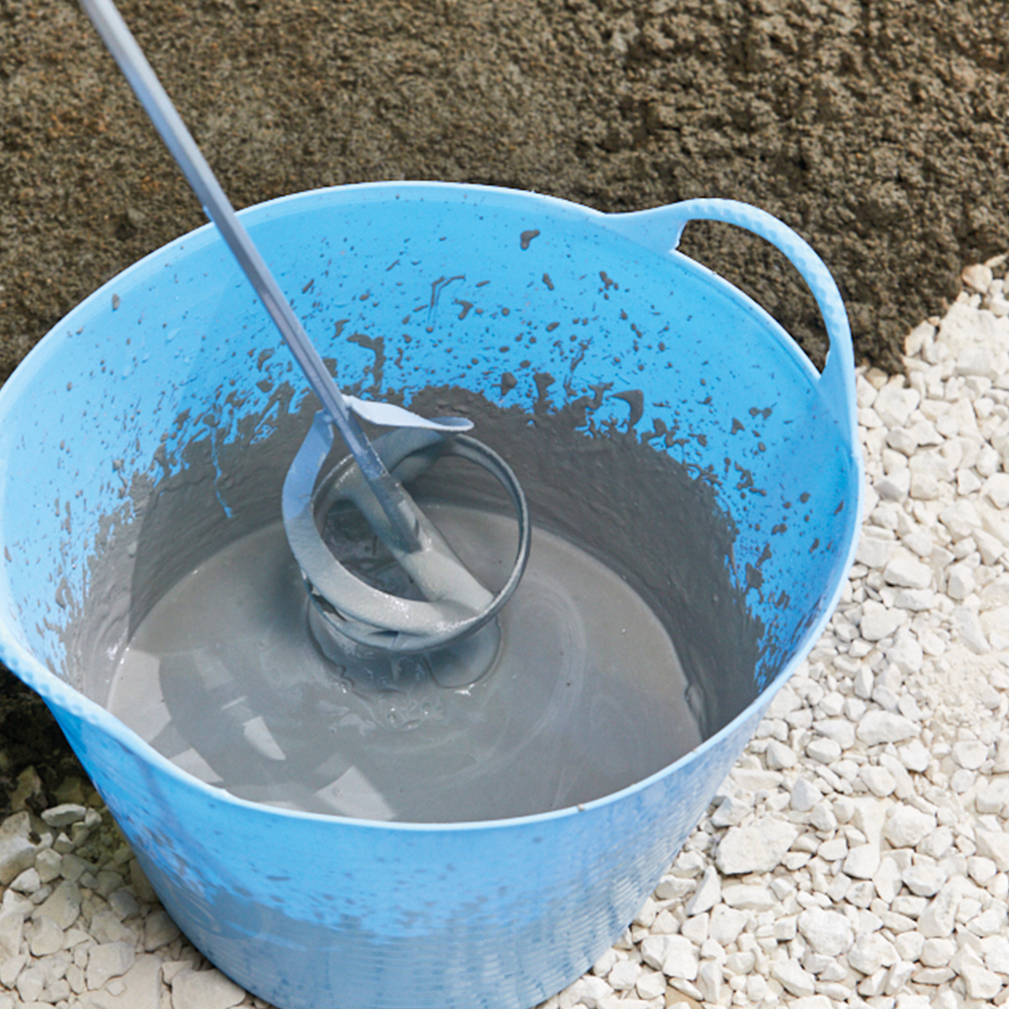 A blue bucket containing mixed bonding slurry with a mixing tool, used for paving preparation.