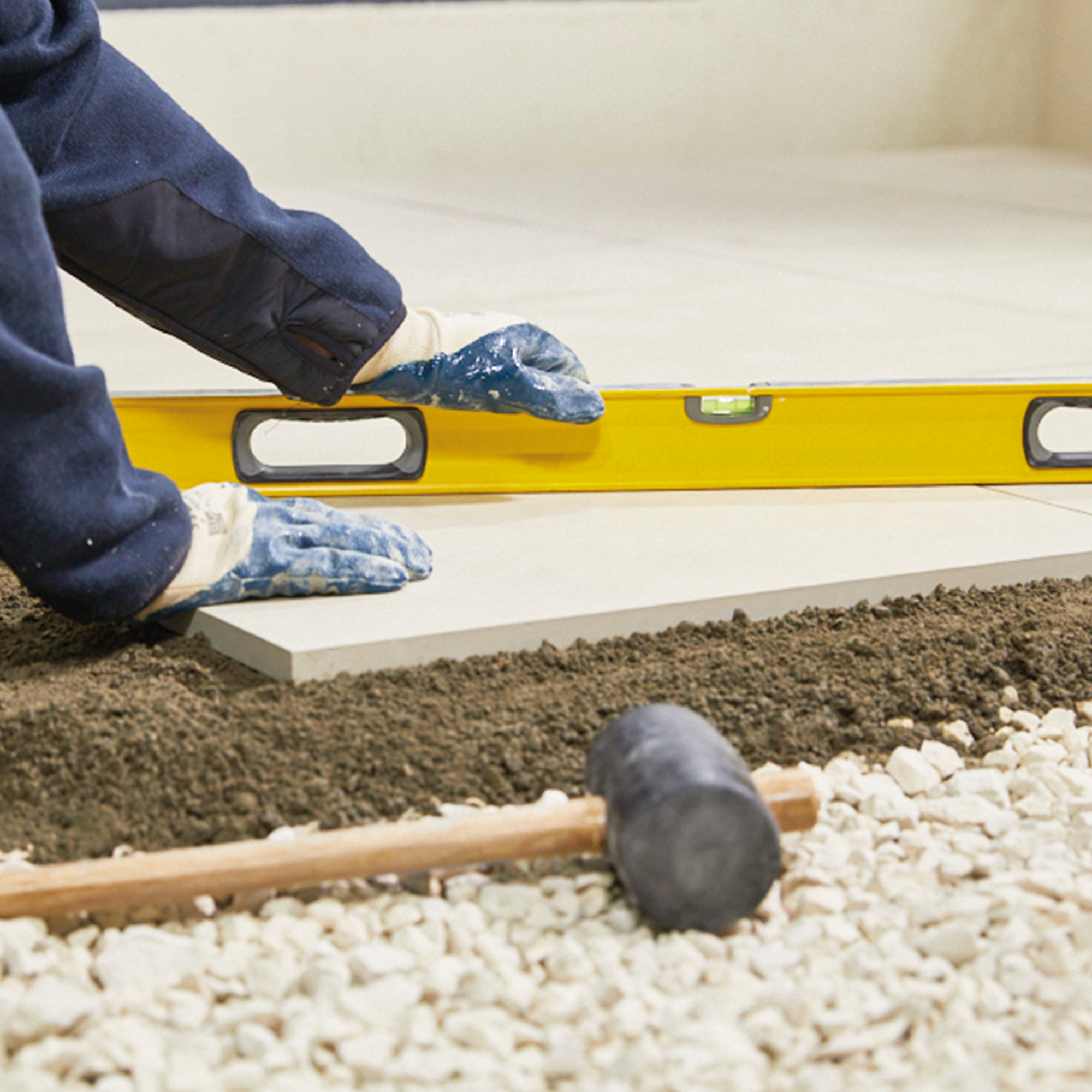 Person using a spirit level to lay paving slabs on prepared ground.