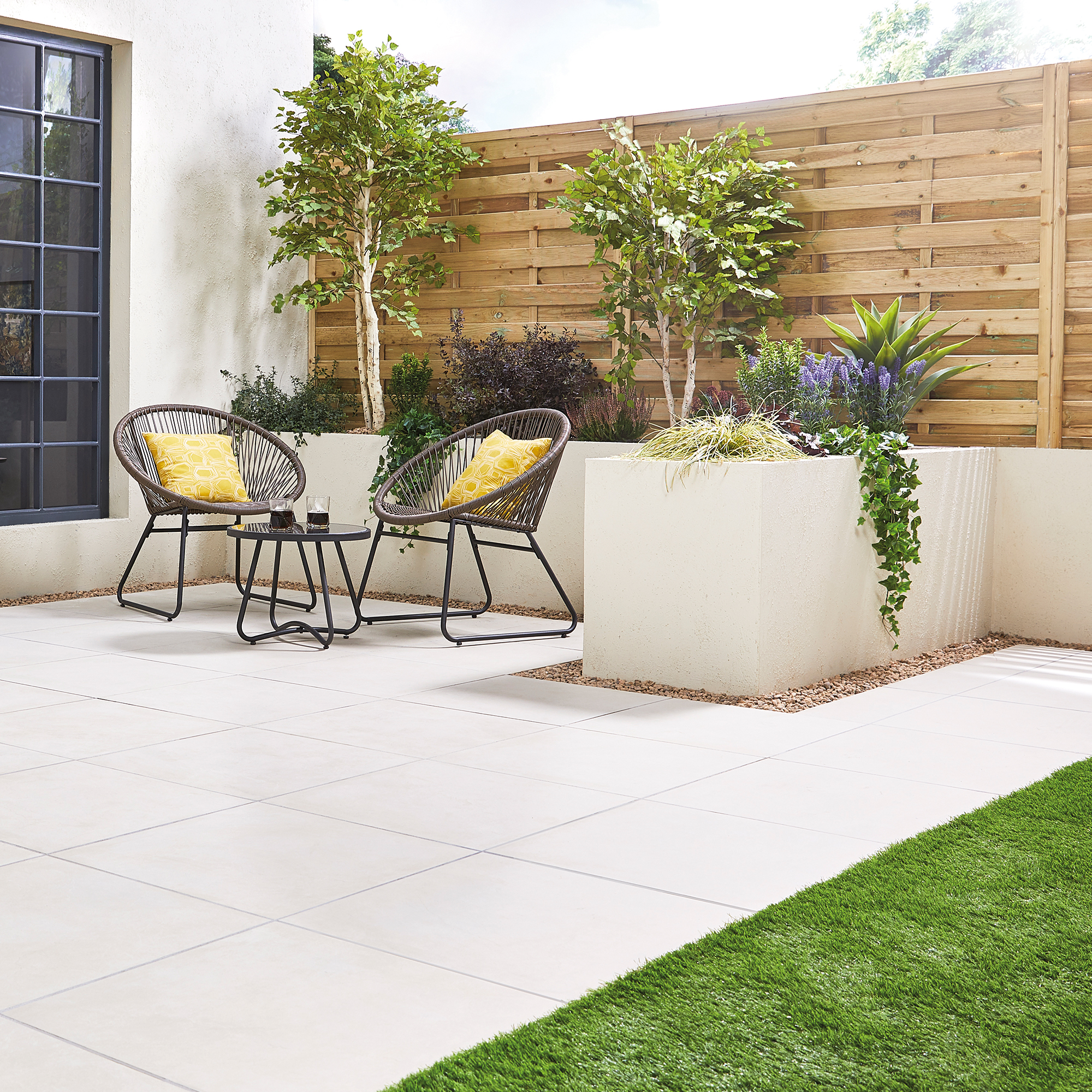 Outdoor patio with modern furniture and lush plants on a tiled surface.