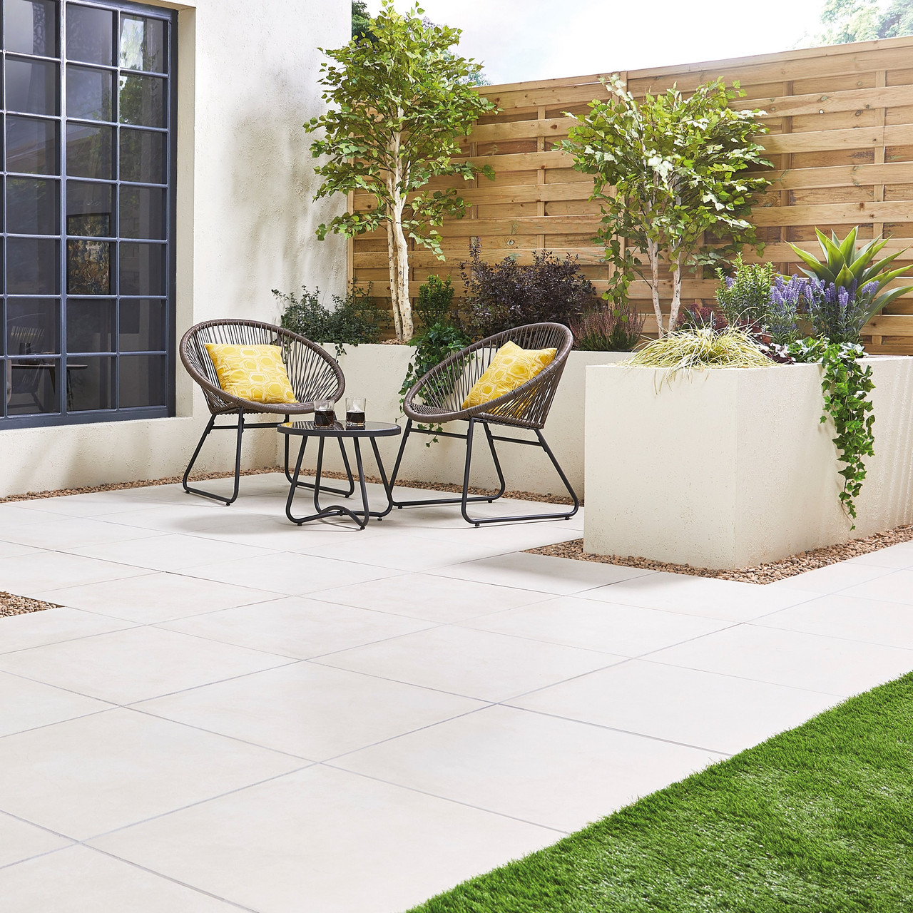 Outdoor patio with light grey porcelain paving and garden furniture.