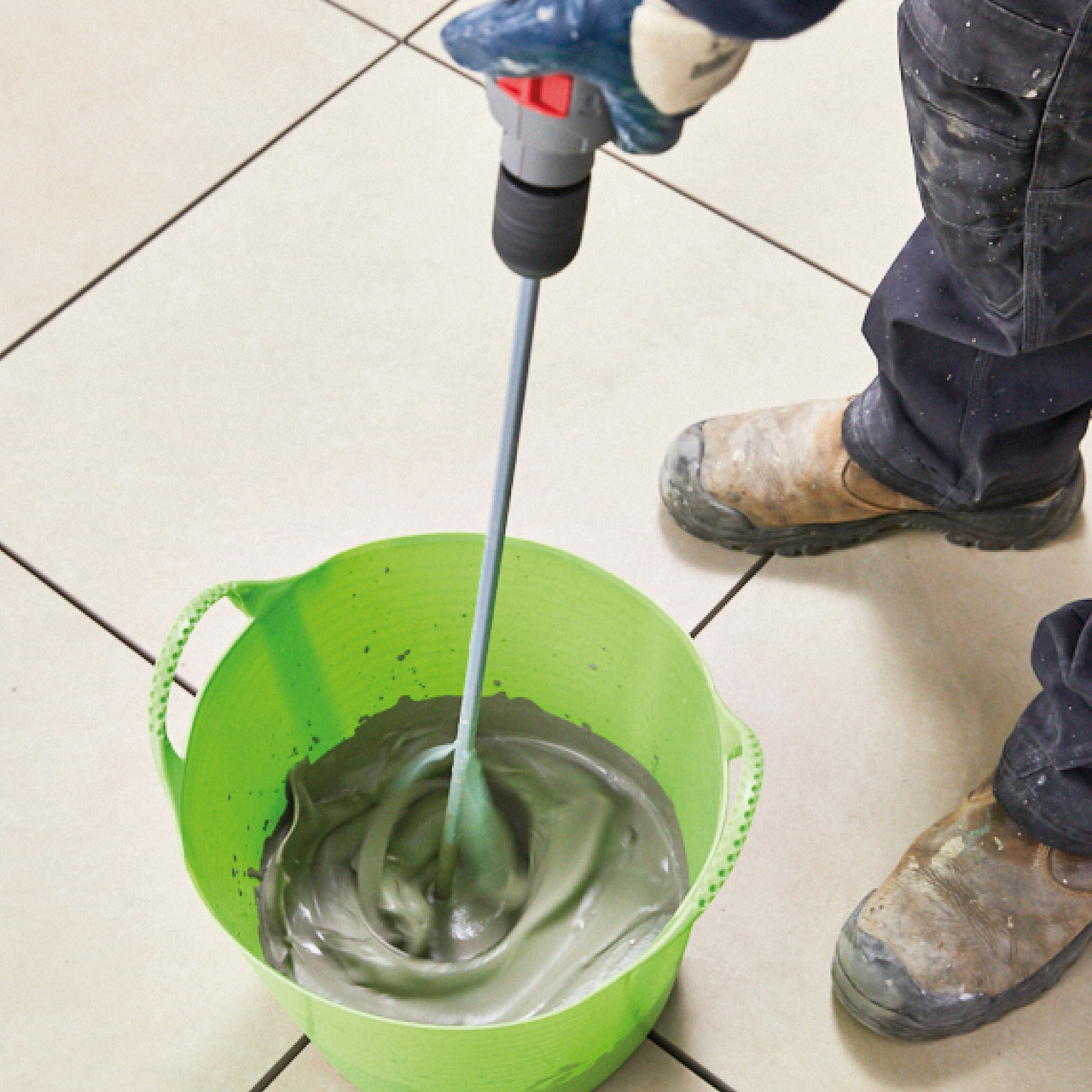 Person mixing light grey porcelain paving jointing compound in a green bucket.
