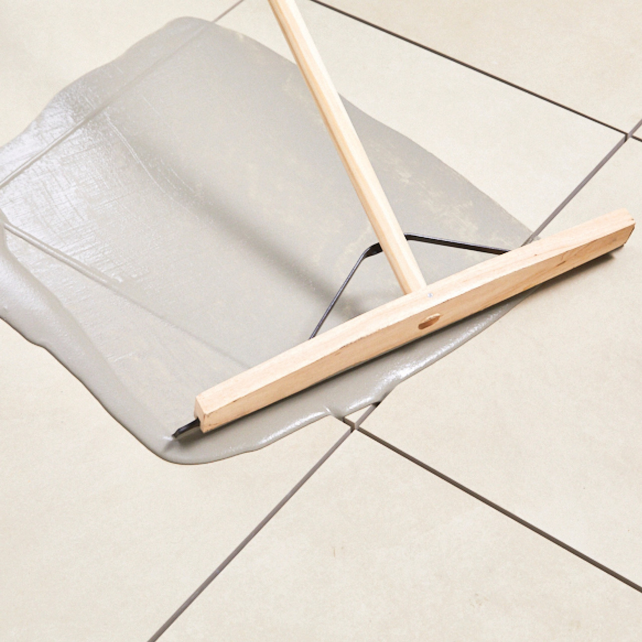 Ivory porcelain paving jointing compound being applied with a wooden tool on tiled surface.