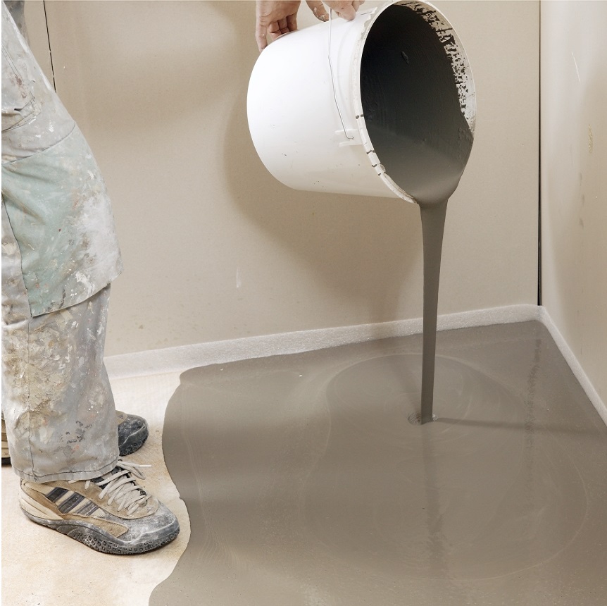 Person pouring self-levelling compound onto a floor surface from a white bucket.