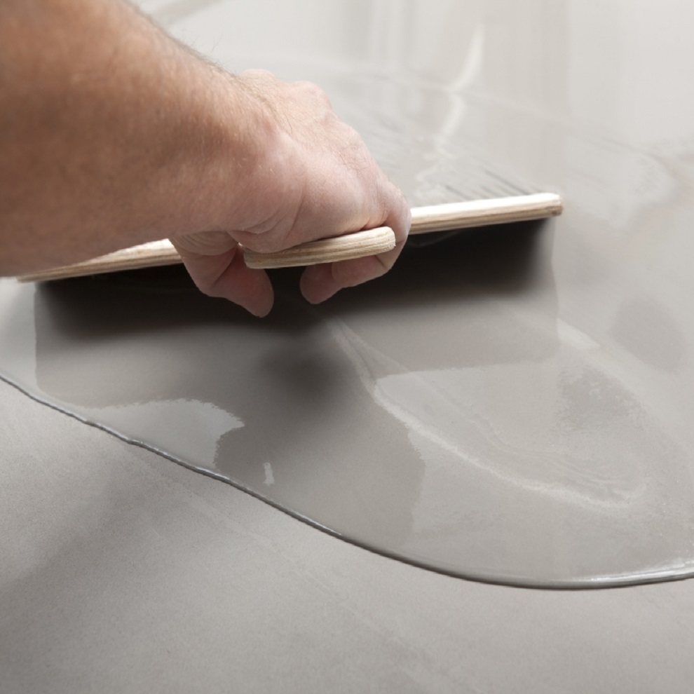 A person using a tool to spread self-levelling compound on a floor surface.