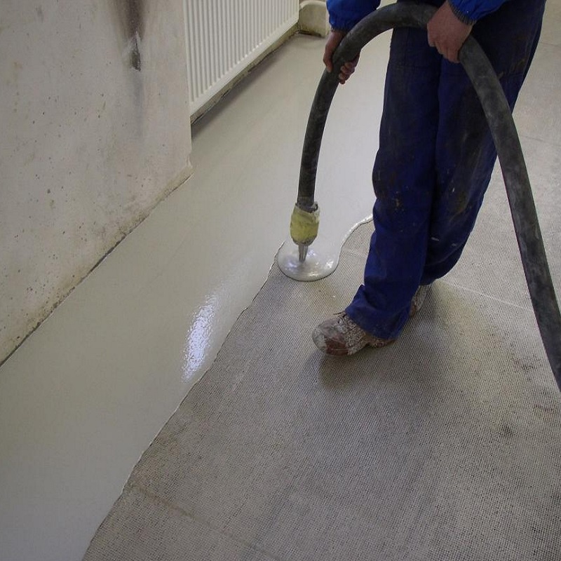 Person applying a self-levelling compound on a floor with a hose.