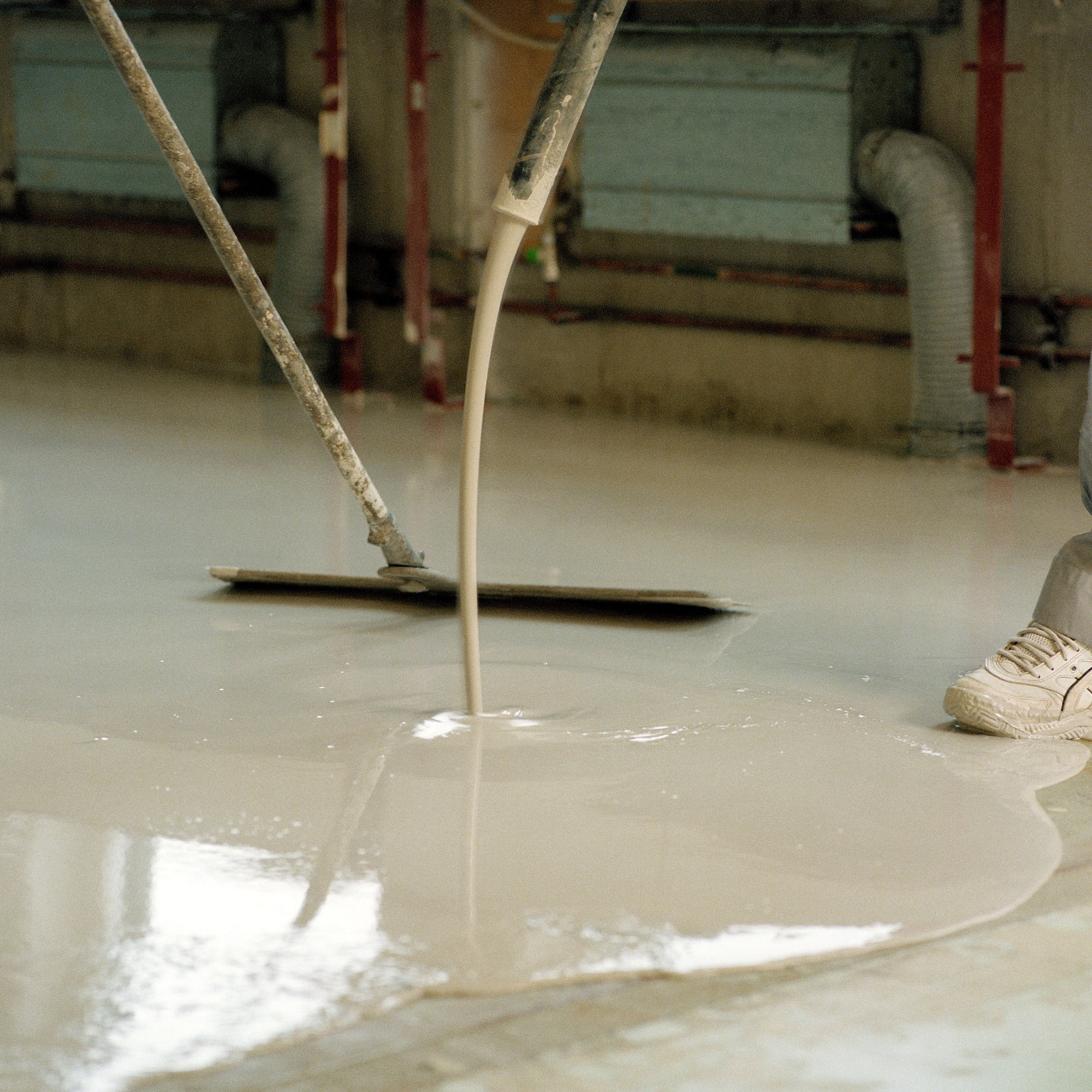 Person applying self-levelling concrete floor compound with a squeegee in an indoor setting.