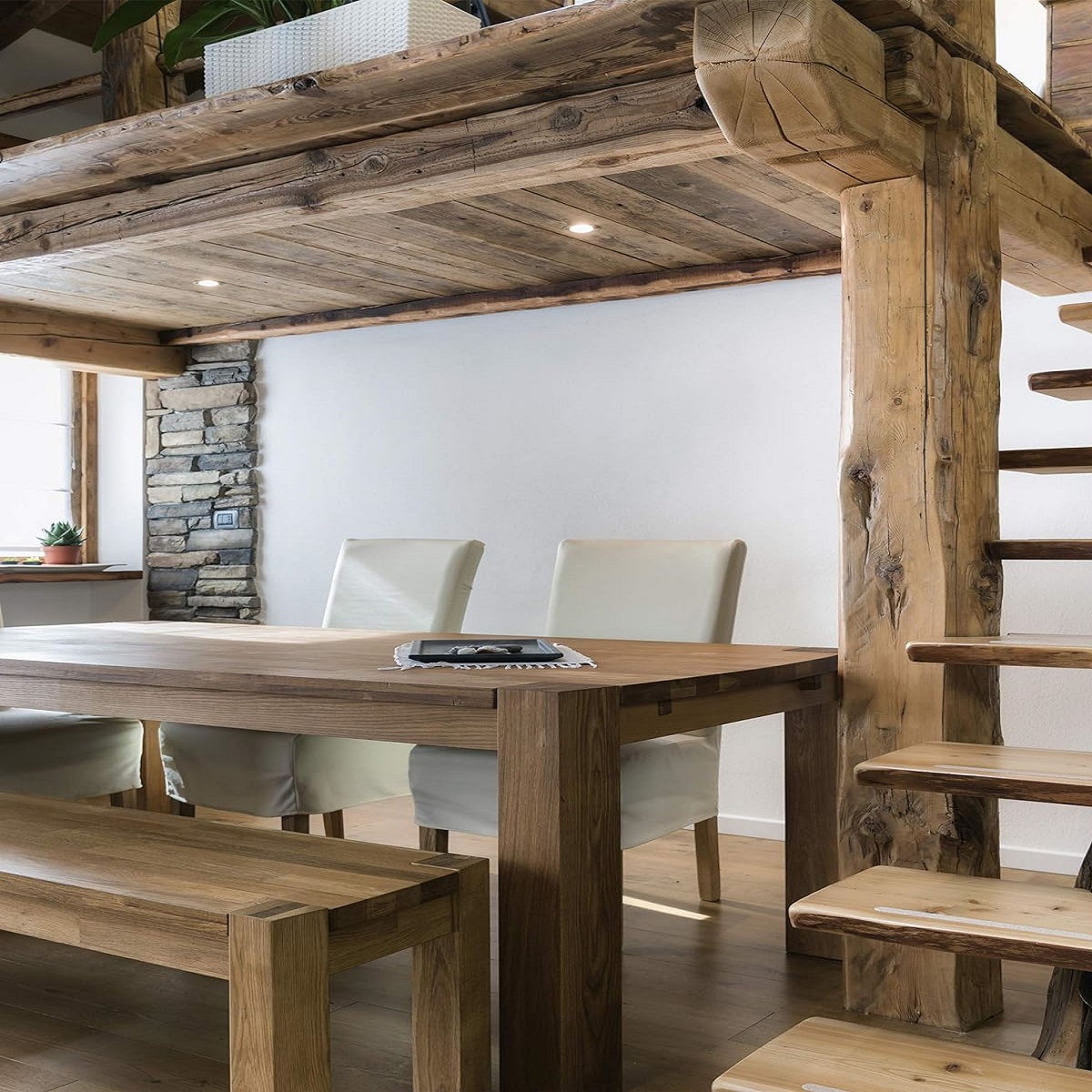 Interior view of a wooden dining table and chairs with exposed wooden beams and staircase.