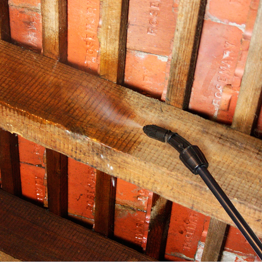 Application of wood treatment on wooden beams with a spray nozzle.