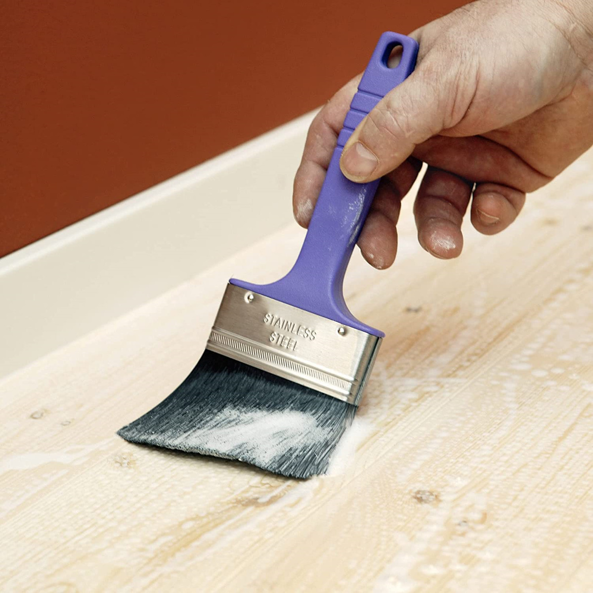 Hand applying wood treatment with a brush on wooden surface