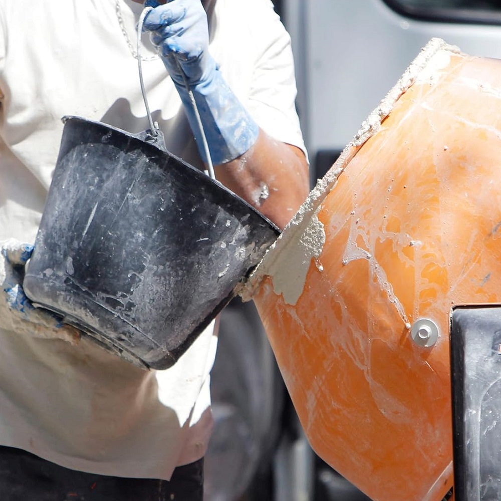 Person mixing mortar with a bucket and concrete mixer.