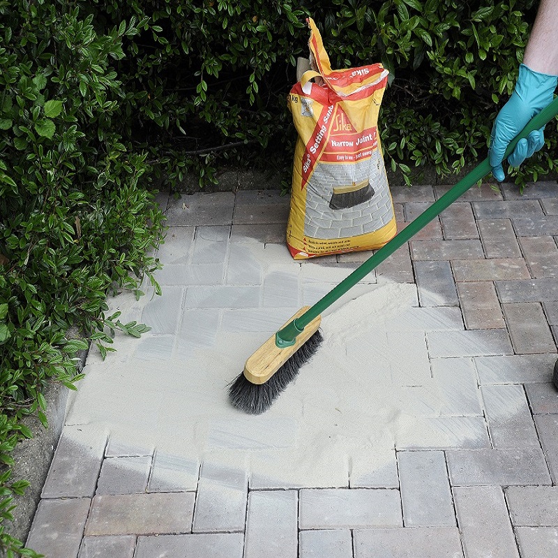 Person using a broom to spread Sika Setting Sand Block Paving Narrow Joint Filler on paving stones.