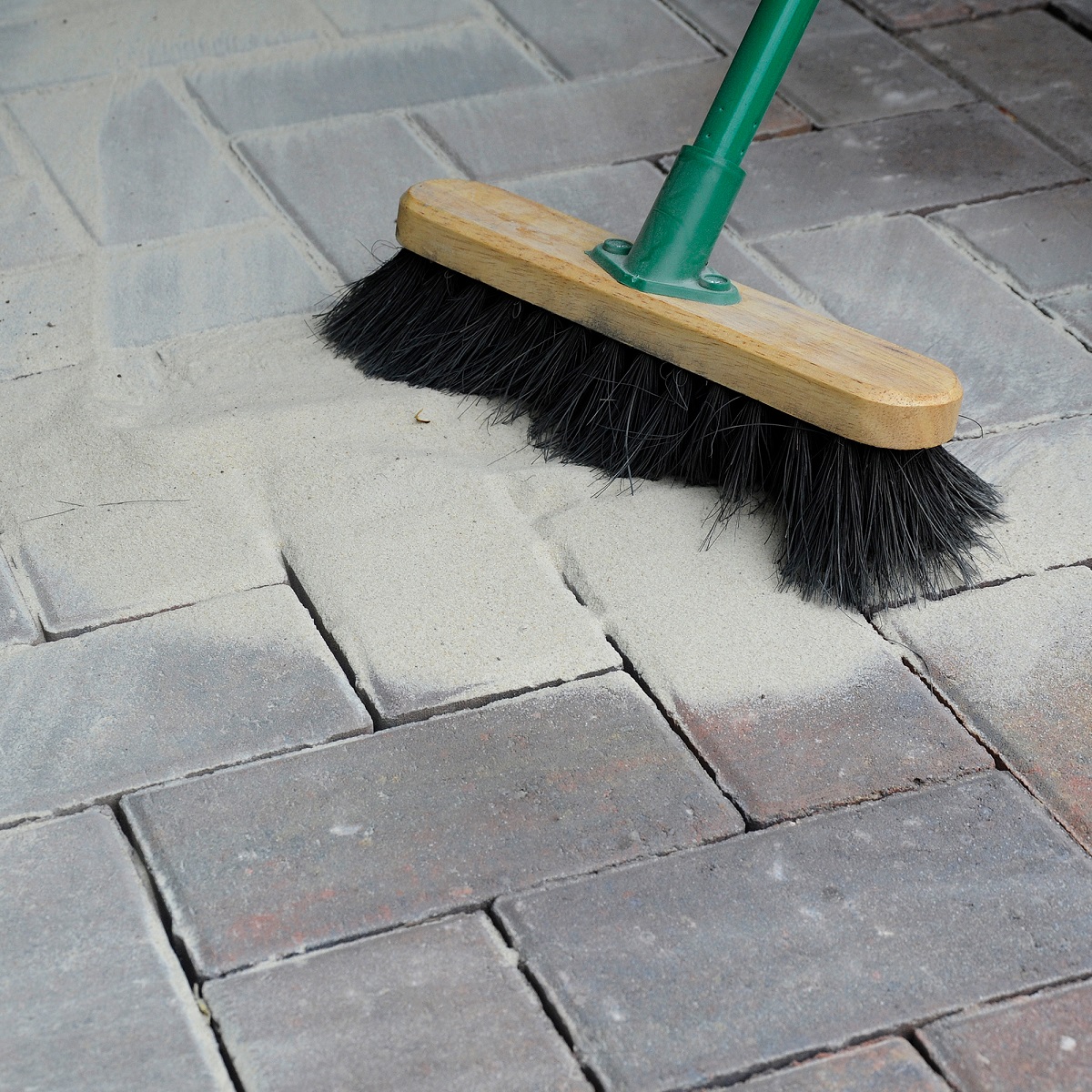 A brush spreading setting sand over block paving.