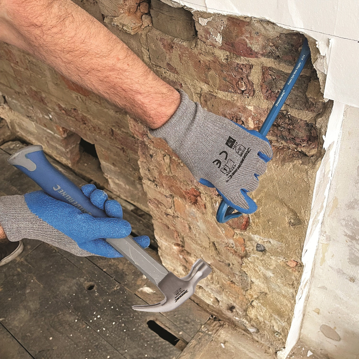 Person wearing blue and white gloves using a hammer and pry bar