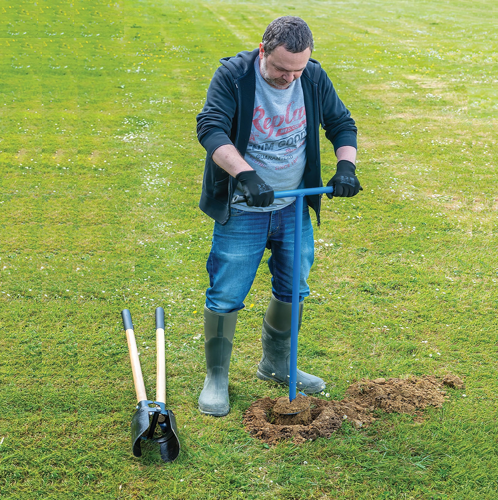 Person using a manual corkscrew fence post hole auger on a grassy field.