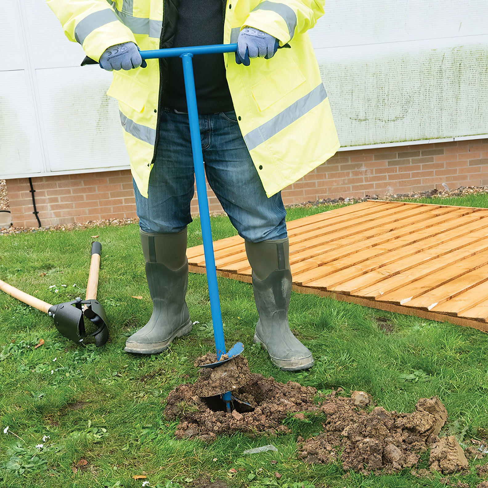 Person using a manual corkscrew fence post hole auger on grassy ground.