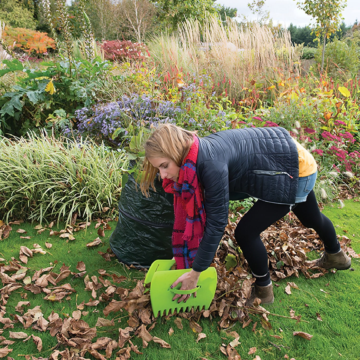 Person using green leaf collector scoops to gather fallen leaves in a garden.