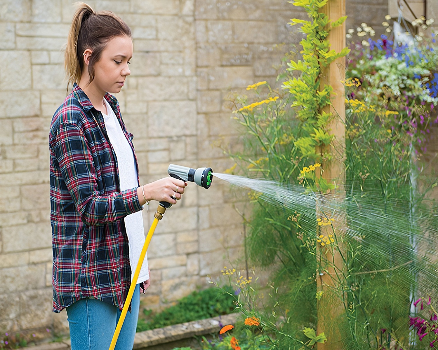 Person using a garden hose with a spray water gun to water plants.