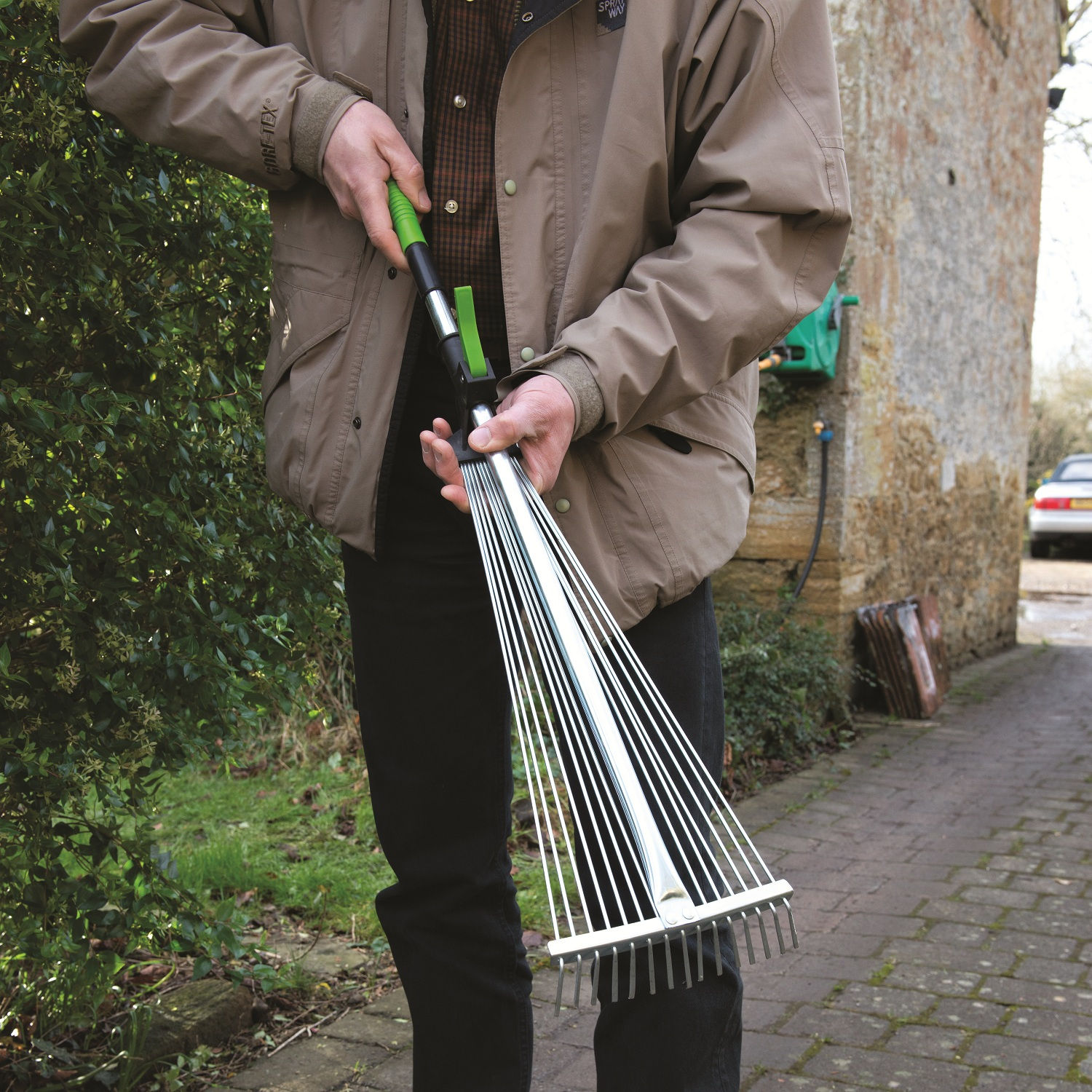 Person using a telescopic adjustable garden leaf and grass rake on a paved path.