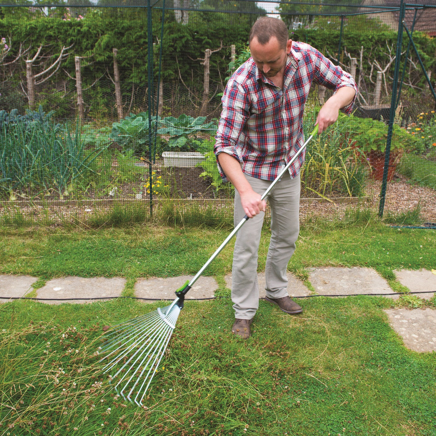 Person using a telescopic adjustable garden leaf and grass rake on a lawn.