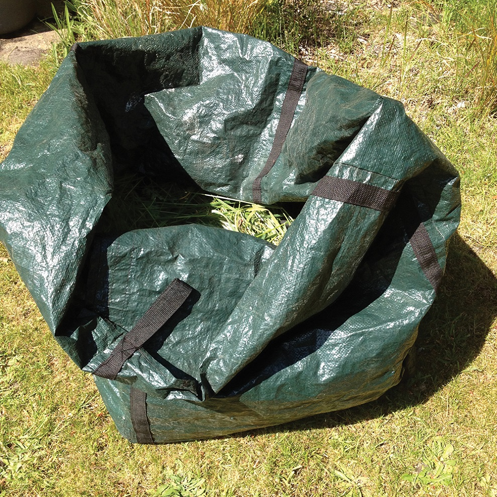 Large green garden refuse sack filled with grass clippings on a lawn.