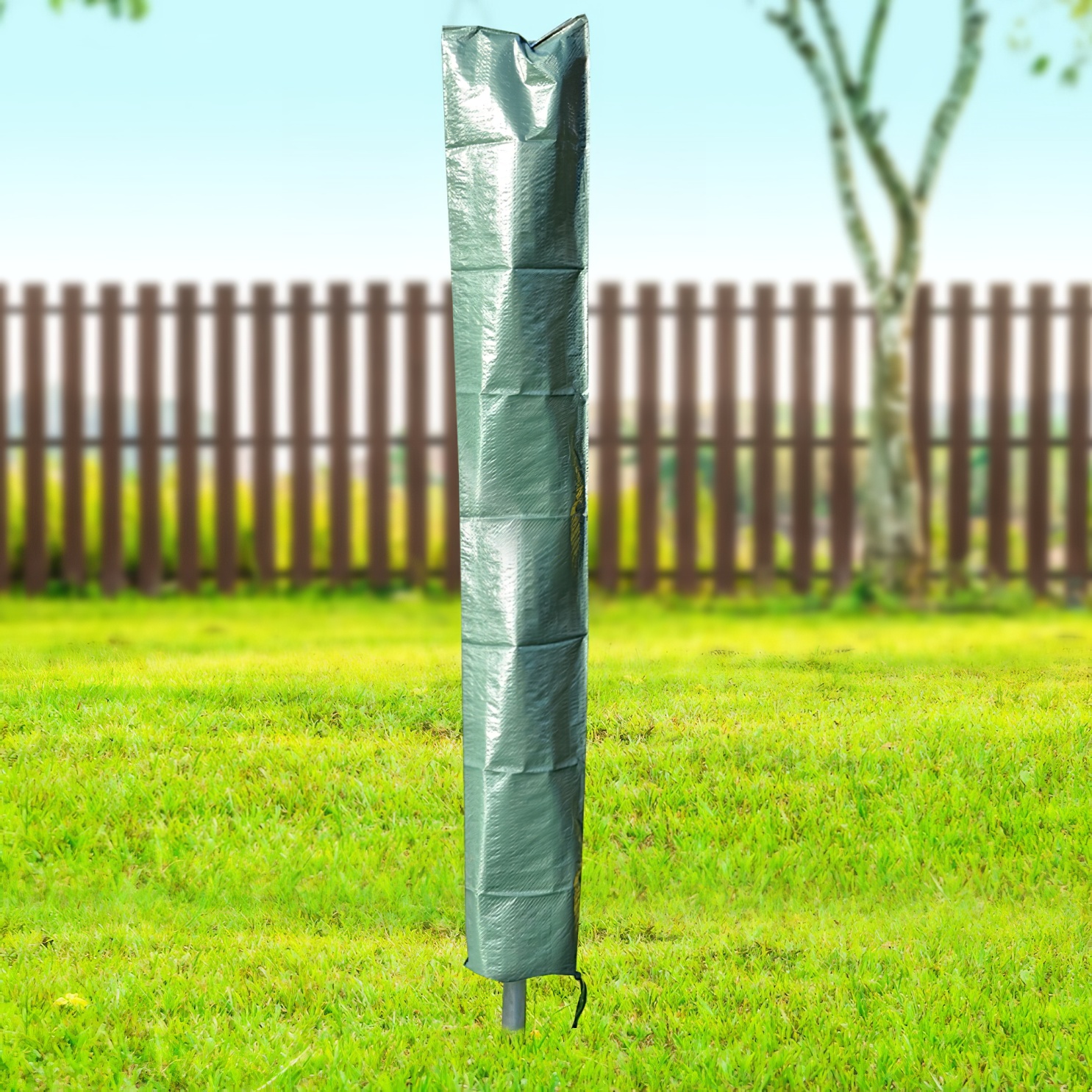 Green garden umbrella cover standing on grass with a wooden fence and trees in the background.