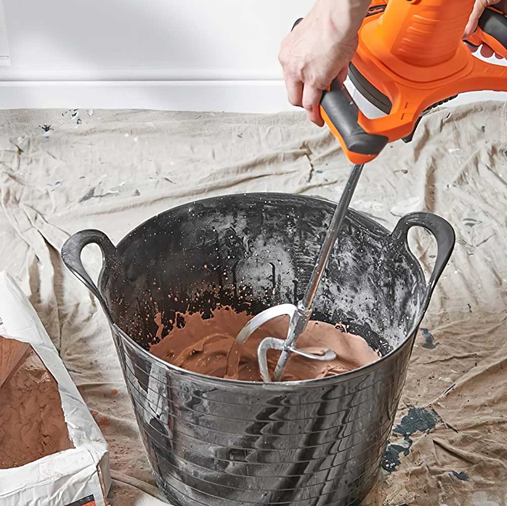 Person using an orange electric power mixer to blend plaster in a black bucket.
