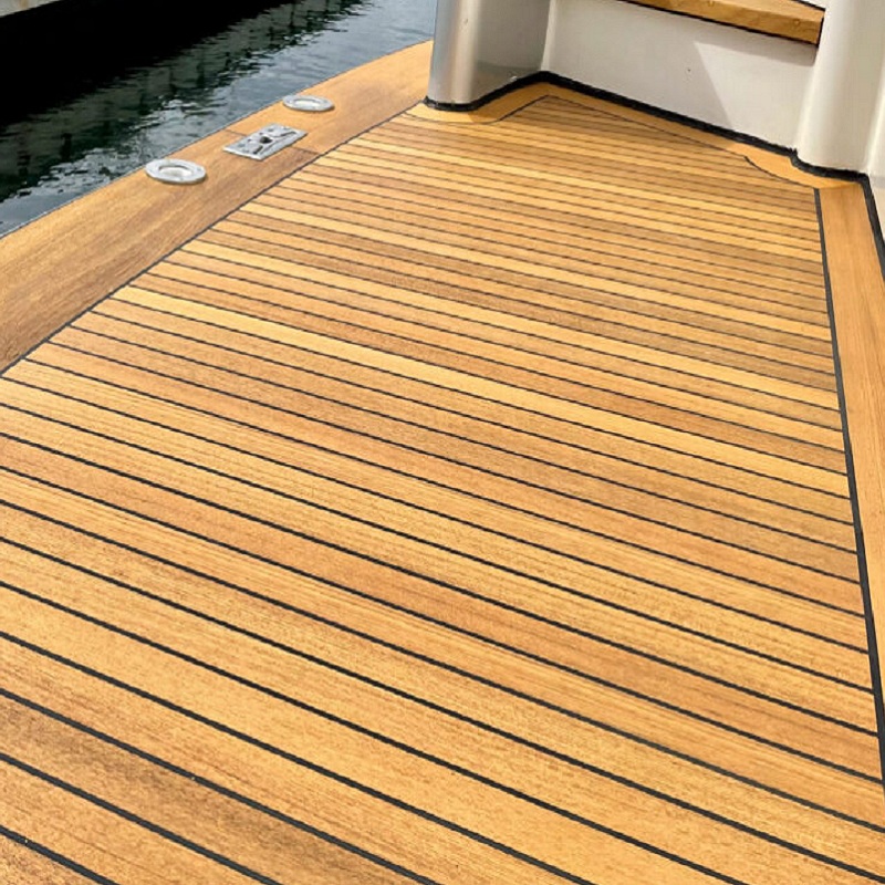 Boat with teak decking before cleaning, moored on calm water.