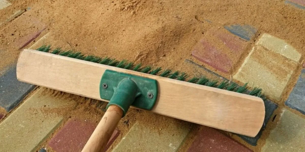 Sweeping sand on patio bricks Broom spreading sand over colourful paving stones