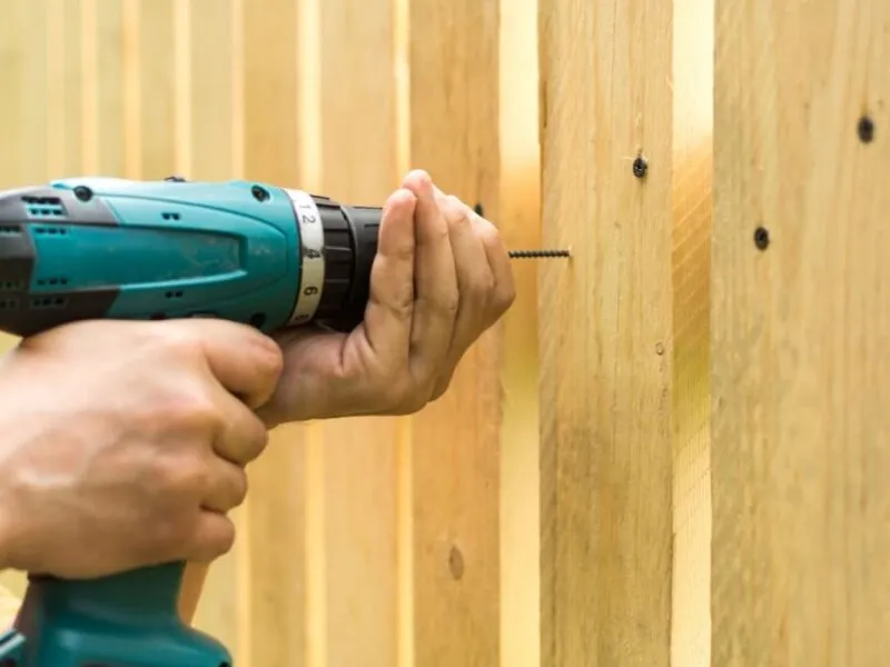Drilling into wooden fence with cordless tool Person using a cordless drill to secure a screw into a wooden fence
