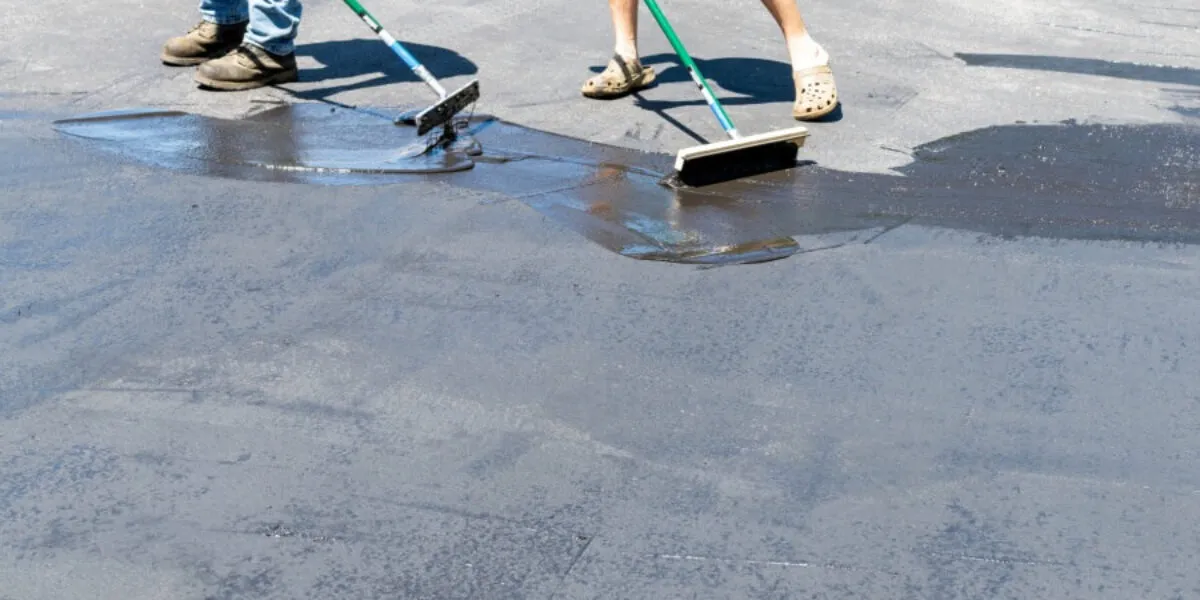 Driveway maintenance with sealant application Two people applying sealant to a driveway with brushes