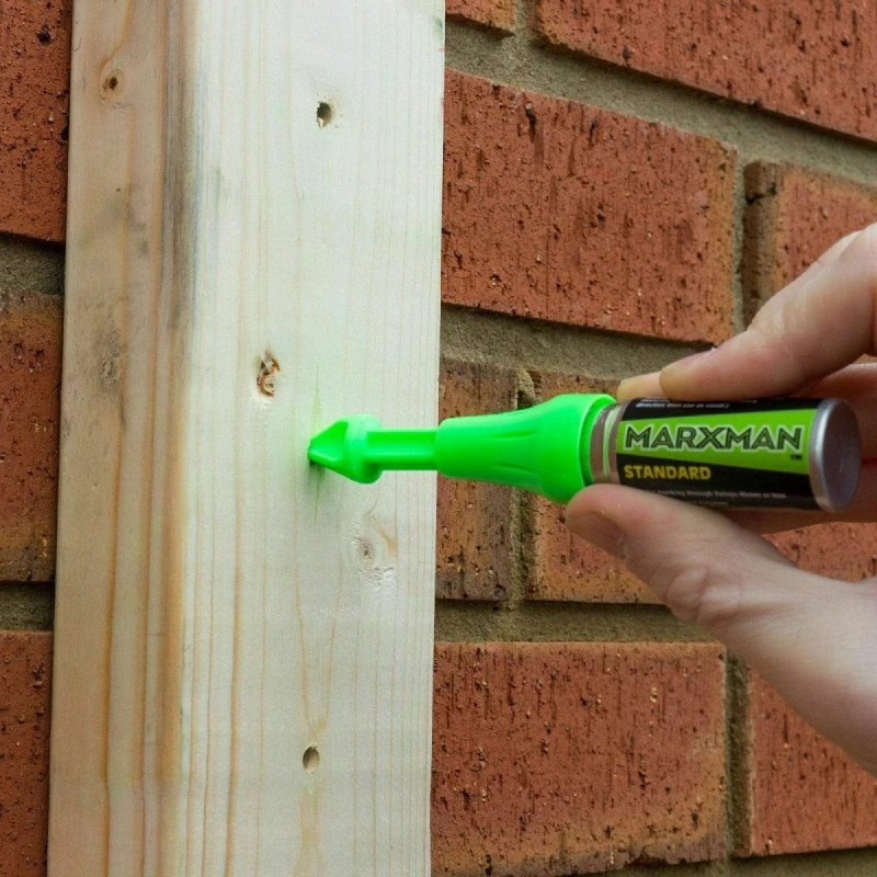 Person marking a wooden board placed against a brick wall using a Marxman tool