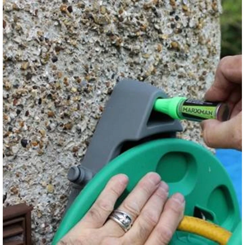 Person using a green Marxman marker to mark holes for fixing a garden hose reel