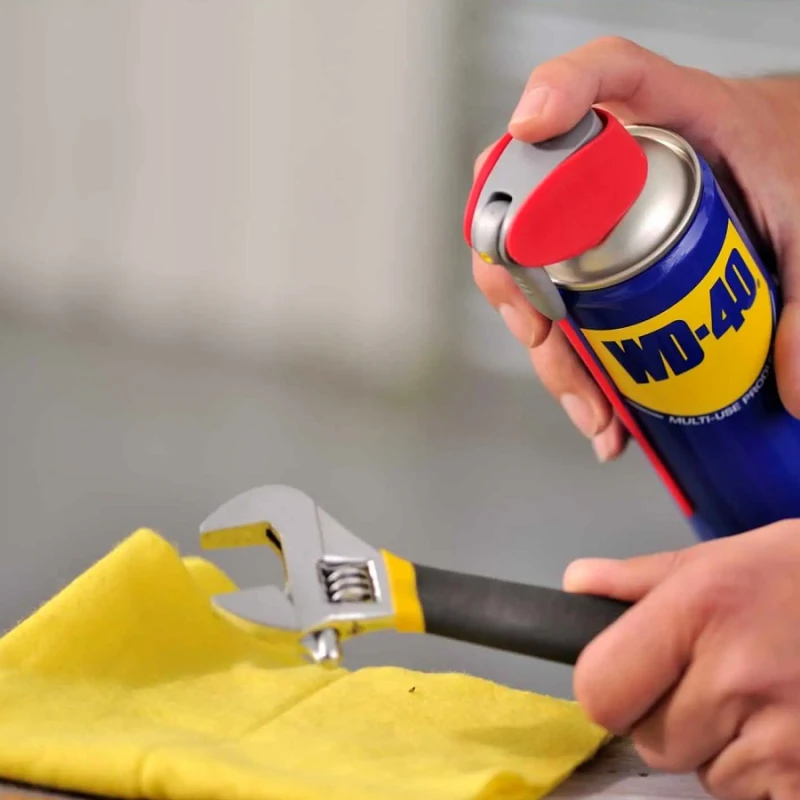 Person applying WD-40 to an adjustable wrench while cleaning with a cloth
