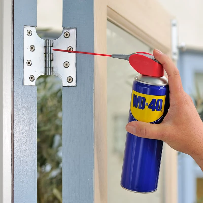 Person using WD-40 spray on a door hinge to stop squeaking and prevent rust