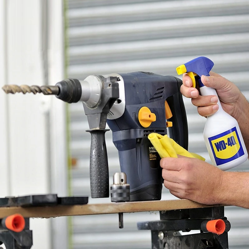Person using WD-40 spray and cloth to clean dust and grime from a cordless drill
