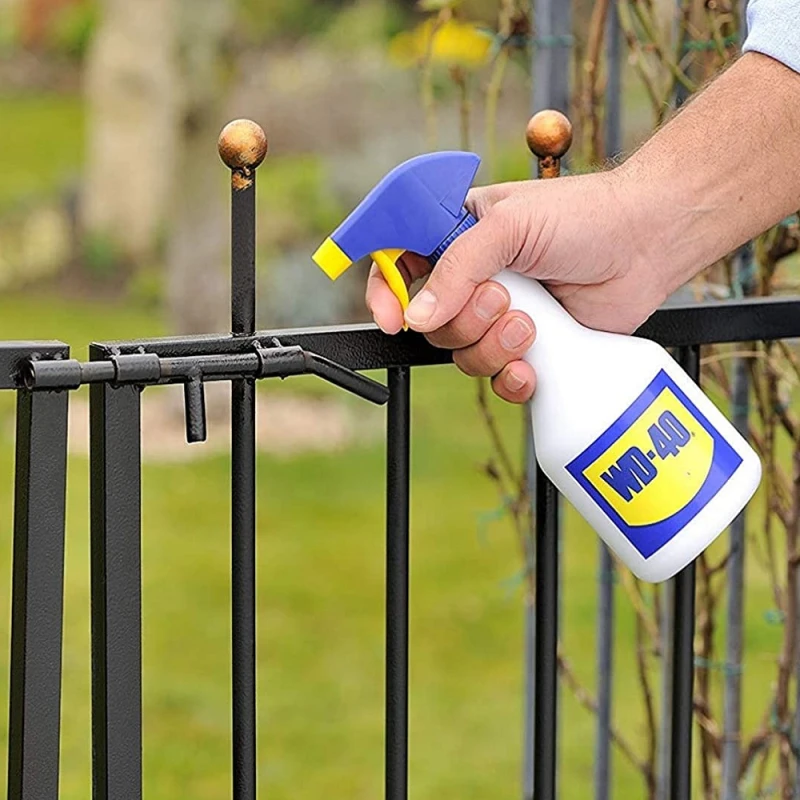 Person applying WD-40 to a garden gate hinge and latch to loosen movement and prevent corrosion
