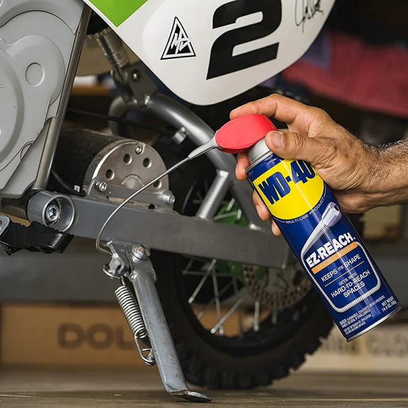 Hand using WD40 Multi-Use Smart Flexible Straw Maintenance Aerosol on a motorbike kickstand.