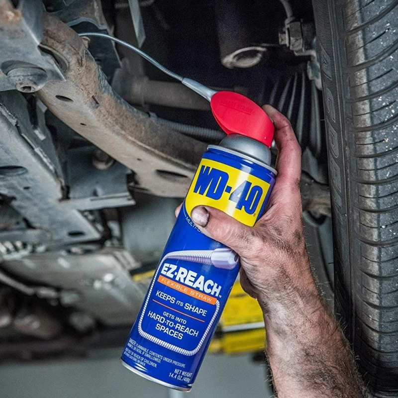 A person using WD40 Multi-Use Smart Flexible Straw Maintenance Aerosol under a vehicle.
