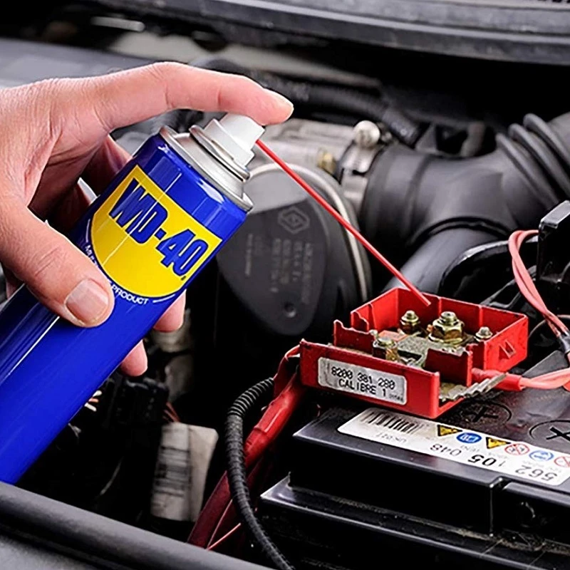 Hand using WD-40 on car engine electrics for cleaning and moisture protection