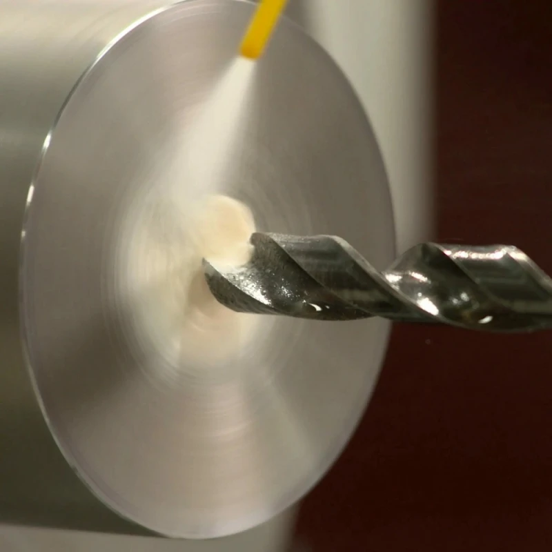 Close-up of a drill bit cutting into metal with WD40 cutting oil spray applied.