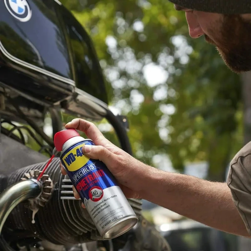 Person using WD40 Specialist Penetrant Fast Release Penetrating Oil on mechanical parts outdoors.