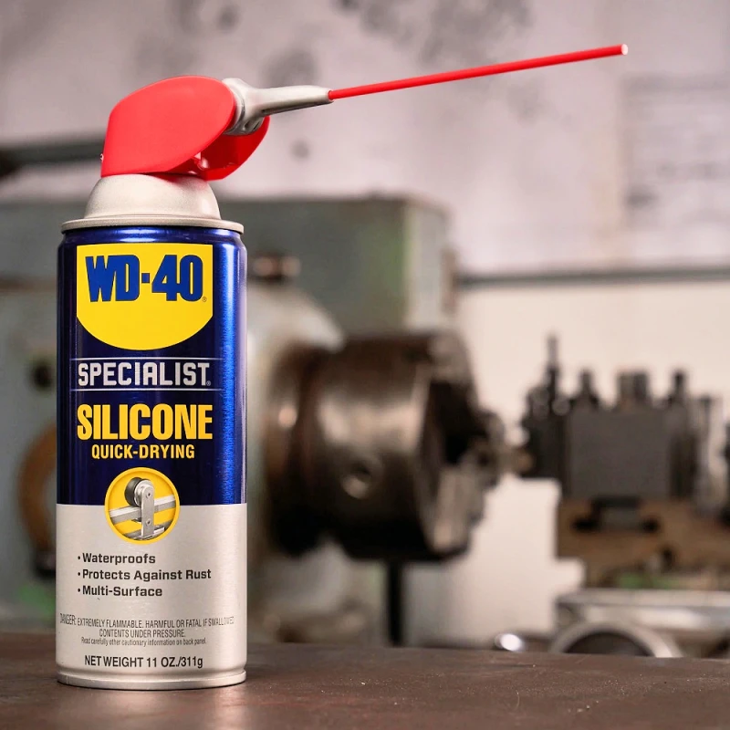 A can of WD40 Specialist High-Performance Silicone Spray with a red straw nozzle, placed on a workshop table.
