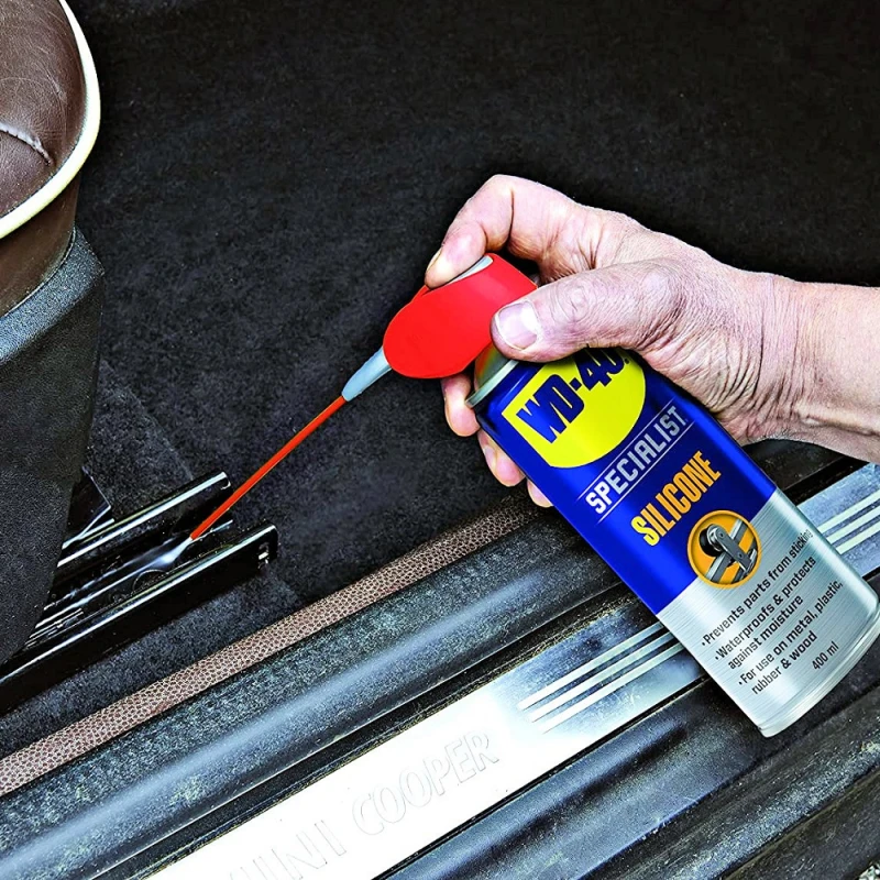 Hand using WD40 Specialist High-Performance Silicone Spray on car seat mechanism.
