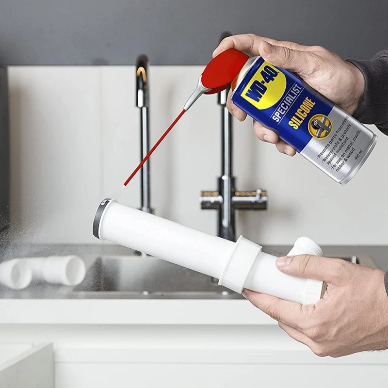 Person using WD40 Specialist High-Performance Silicone Spray on a pipe in a kitchen setting.