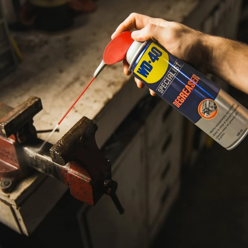 Hand using WD40 Specialist Industrial Strength Degreaser Spray on a metal vice.